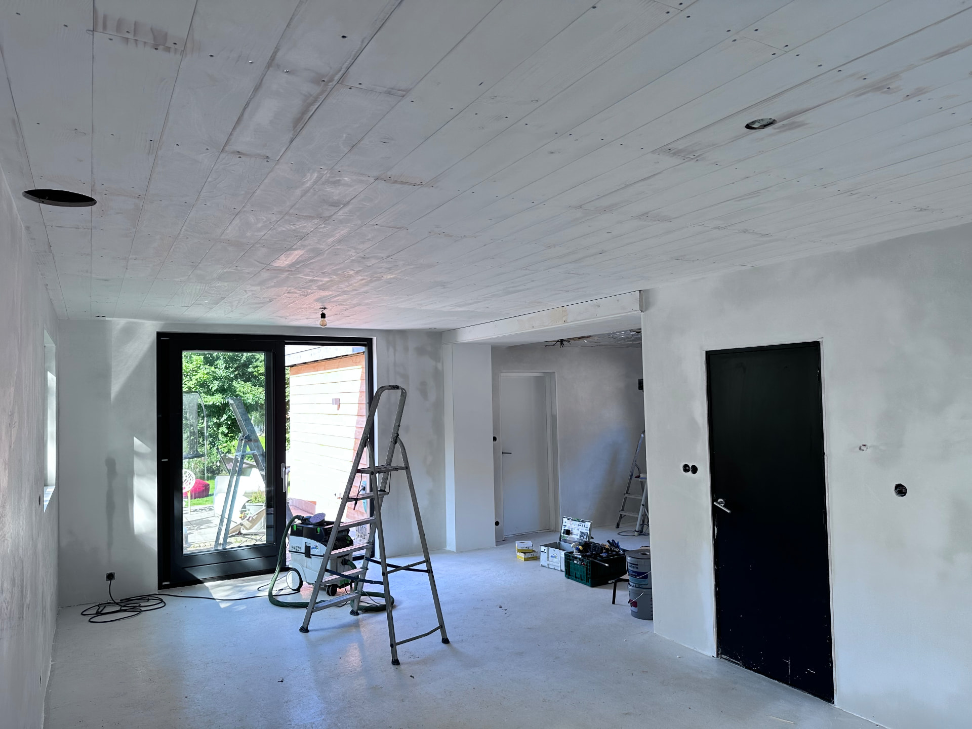 Ruimte tijdens renovatie met voorbereide wanden, een trapladder en schildermateriaal