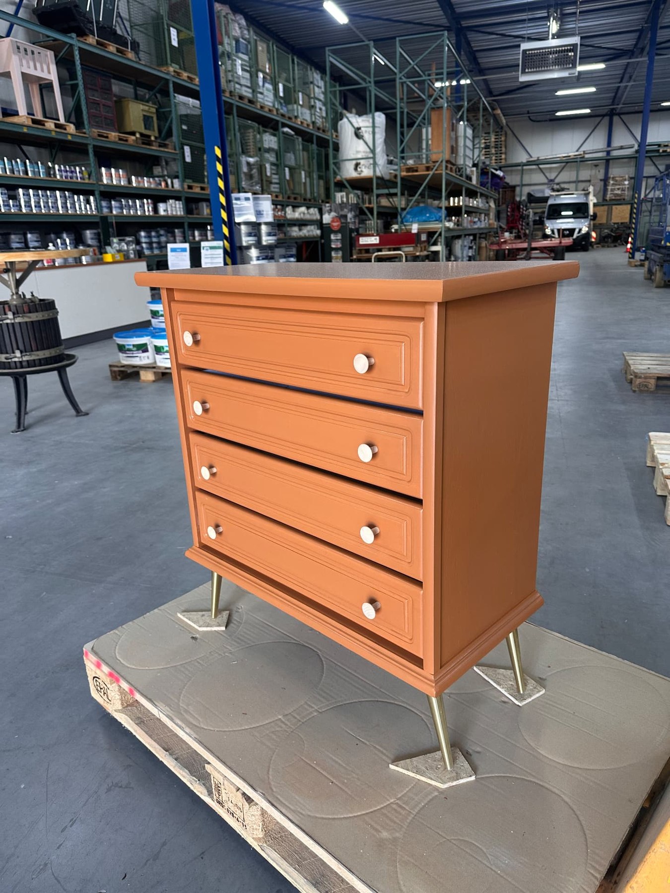 Oranje gespoten ladekast met lichte knoppen en slanke poten