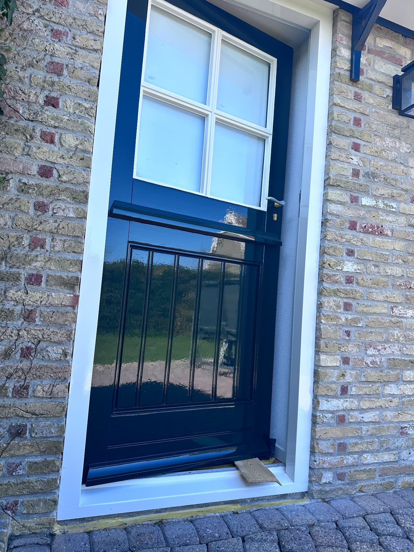 Donkergroene voor-huisdeur met glas bovenin, wit omrand in een gele bakstenen gevel