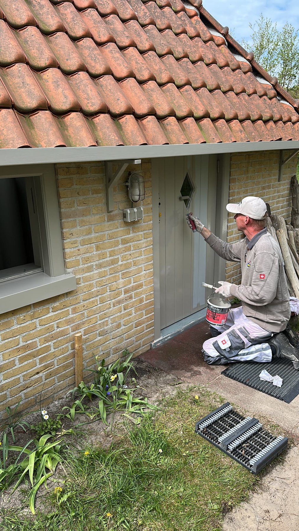 Schilder die met een kwast een grijze buitendeur schildert