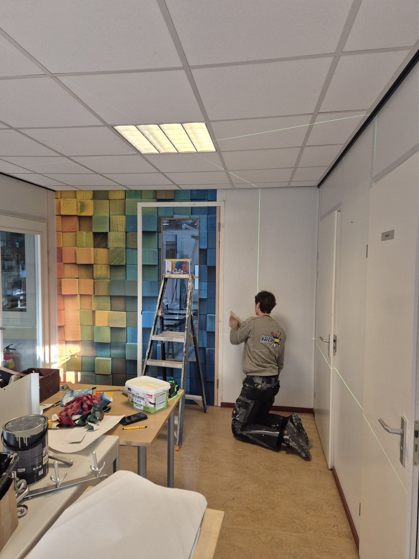 Behanger die met een spatel een wand afwerkt terwijl een groene laserlijn de uitlijning geeft