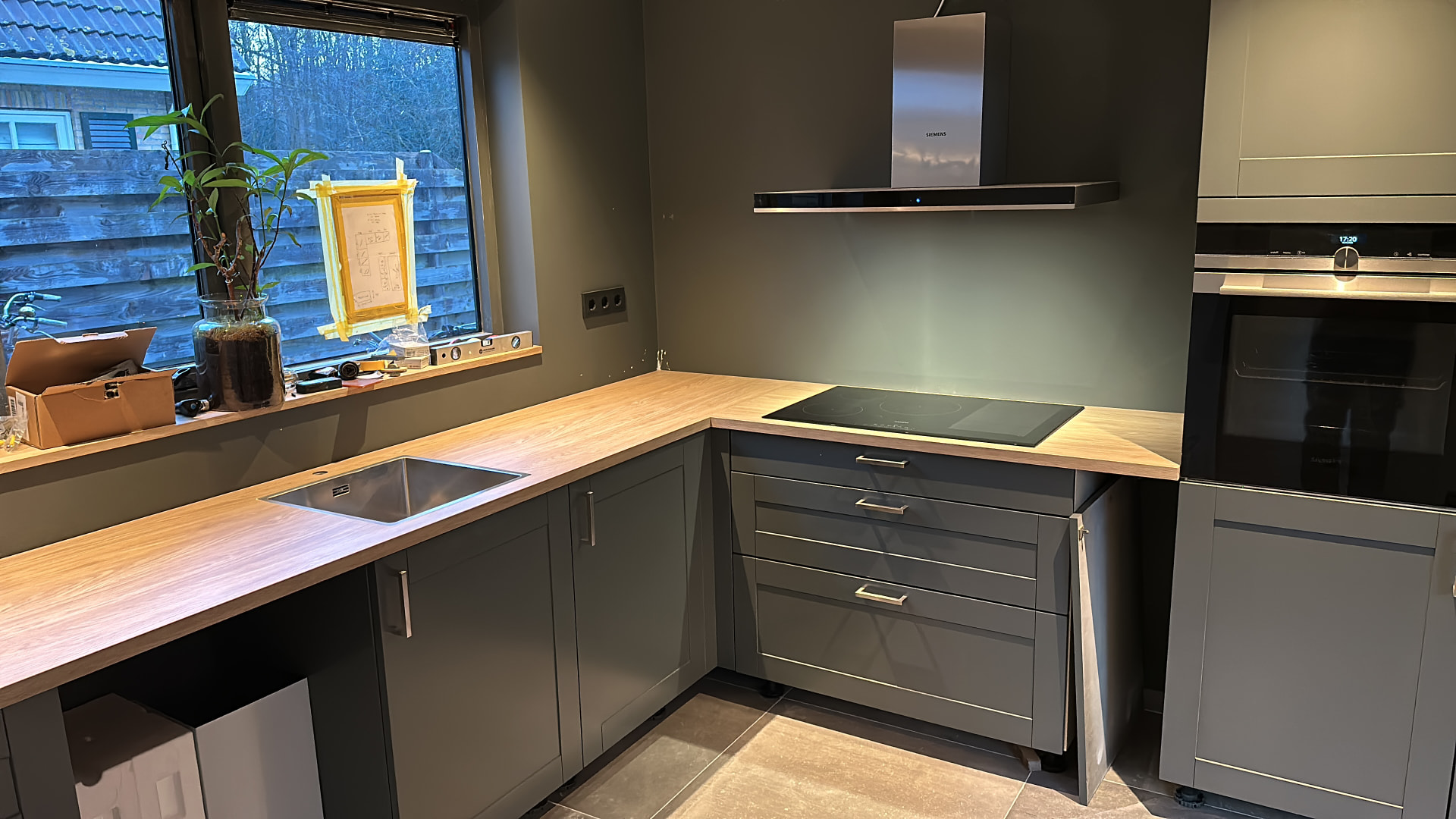 Keuken met grijsgroene wanden, donkere kastfronten en een houten werkblad