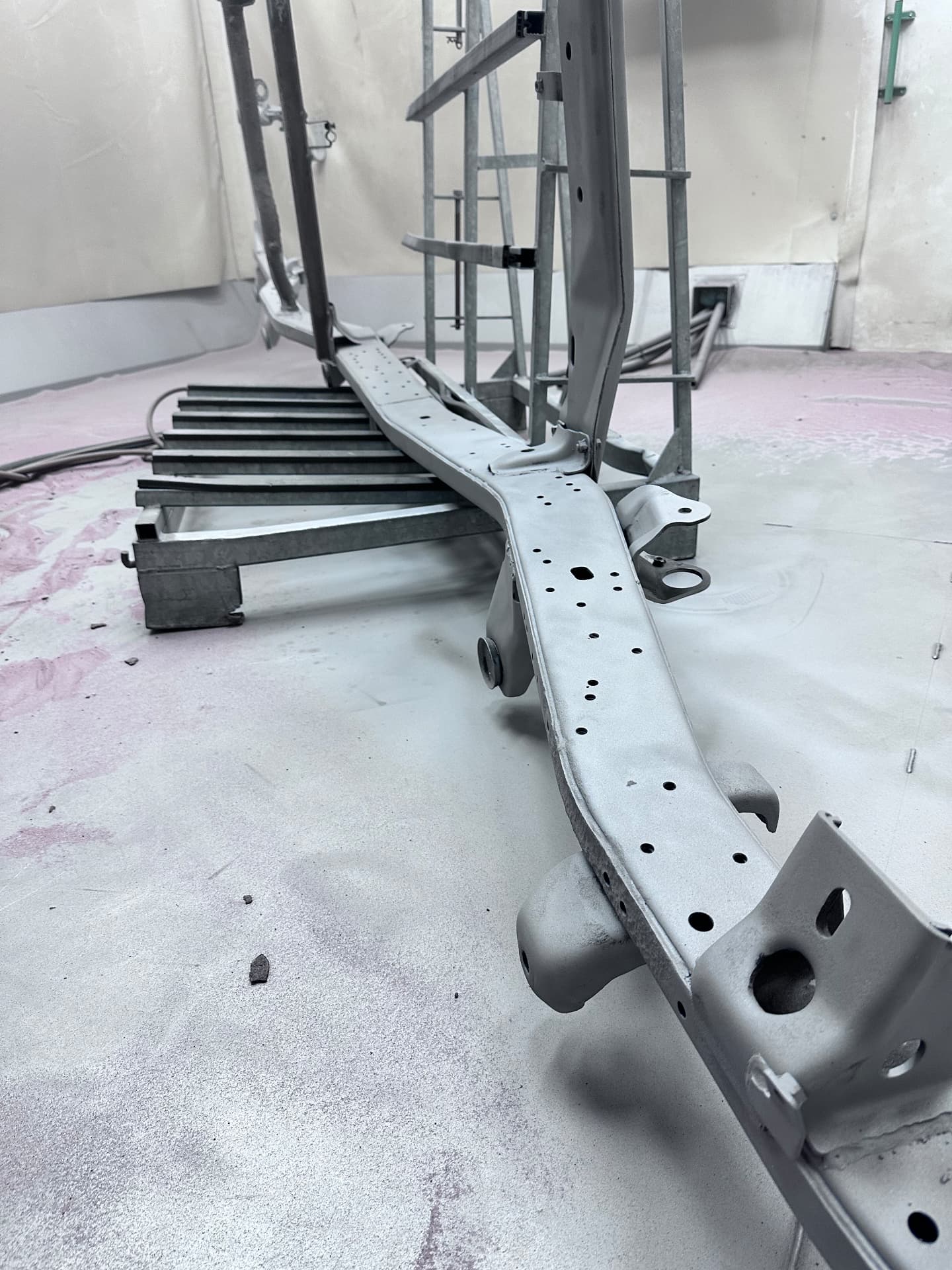 Kaal gestraald ladderchassis van een terreinwagen op bokken in de straalcabine