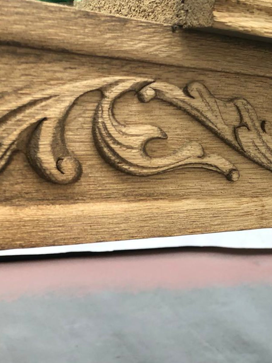 Detail van gestraald houtsnijwerk aan de rand van een tafel van kaal eikenhout