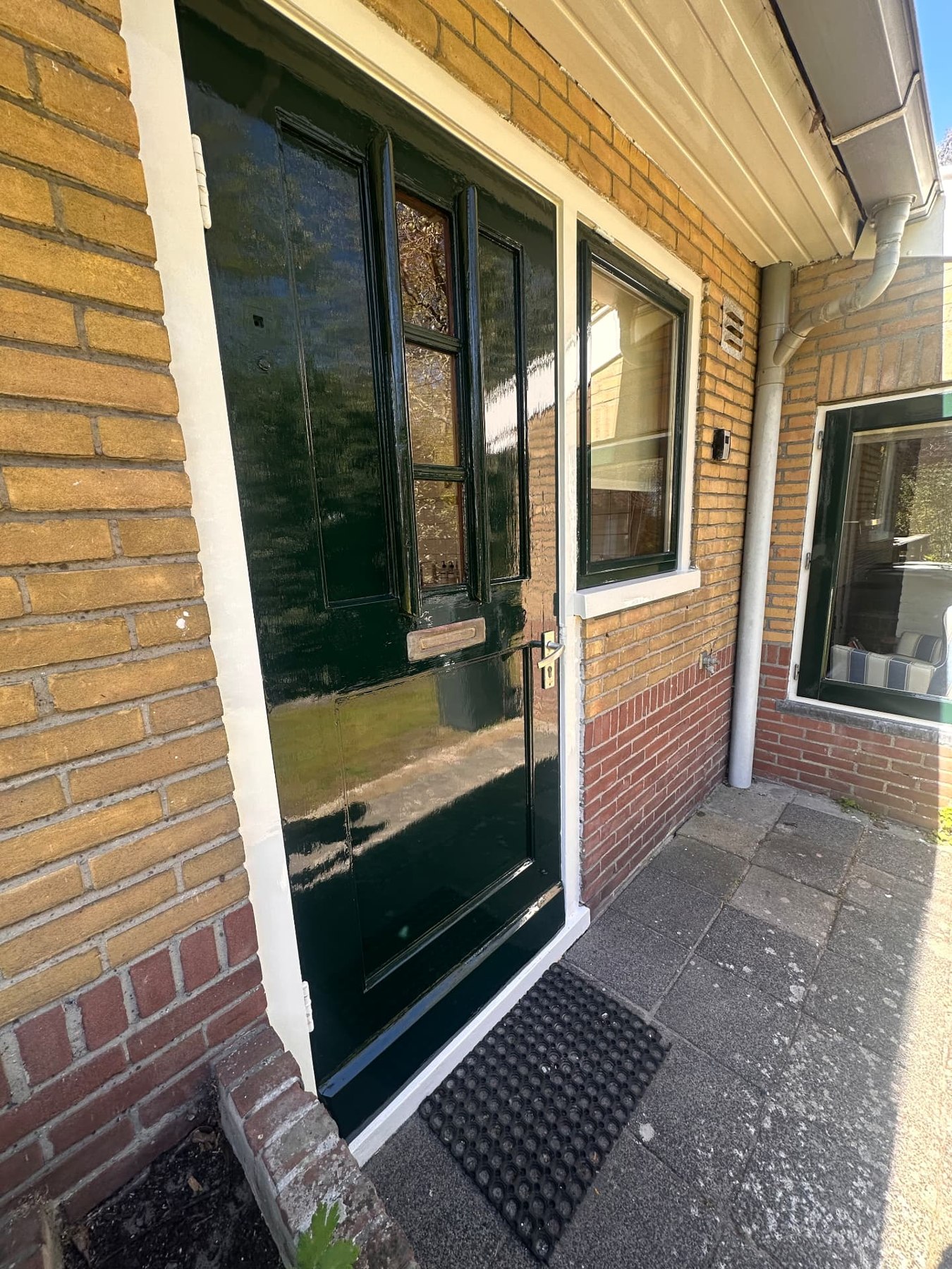Glanzend donkergroene voordeur en raam met witte kozijnen