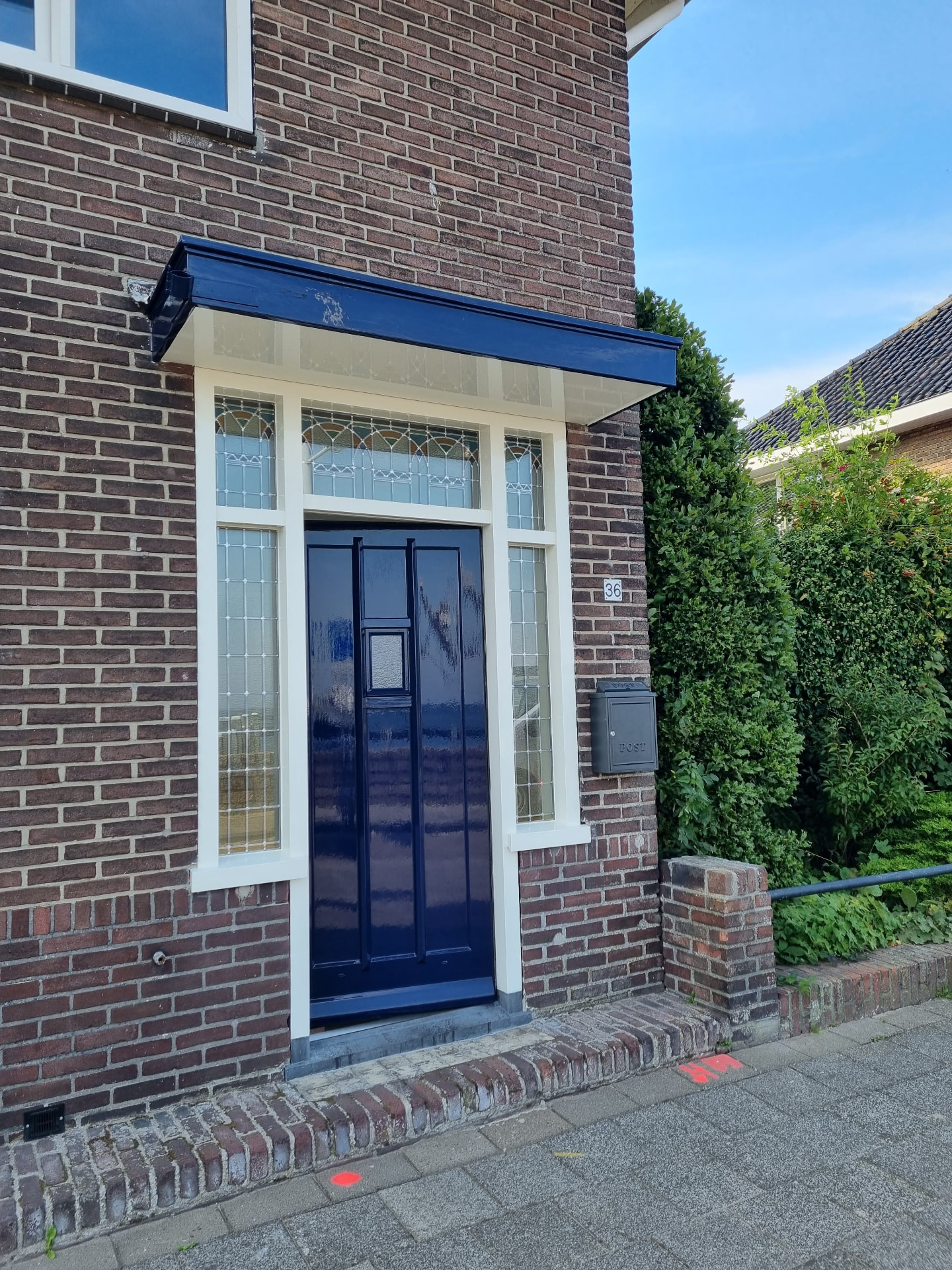 Donkerblauwe voordeur met wit kozijn, glas-in-lood sidelite en blauw geschilderde luifel